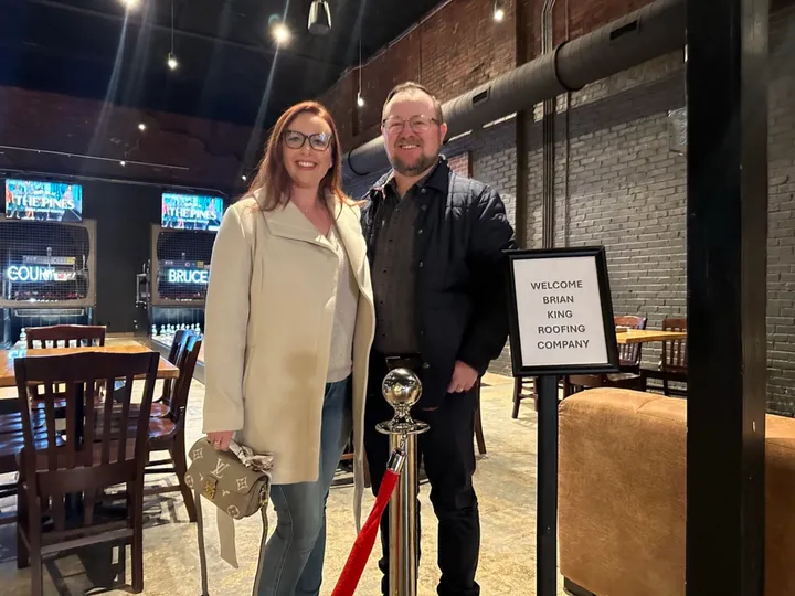 Ryan and Brittany at a company event with a Welcome Brian King Roofing Company sign