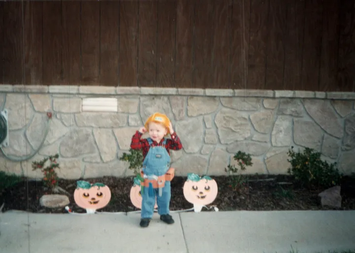 Toddler Ryan in a hard hat and tool belt in front of Halloween pumpkins