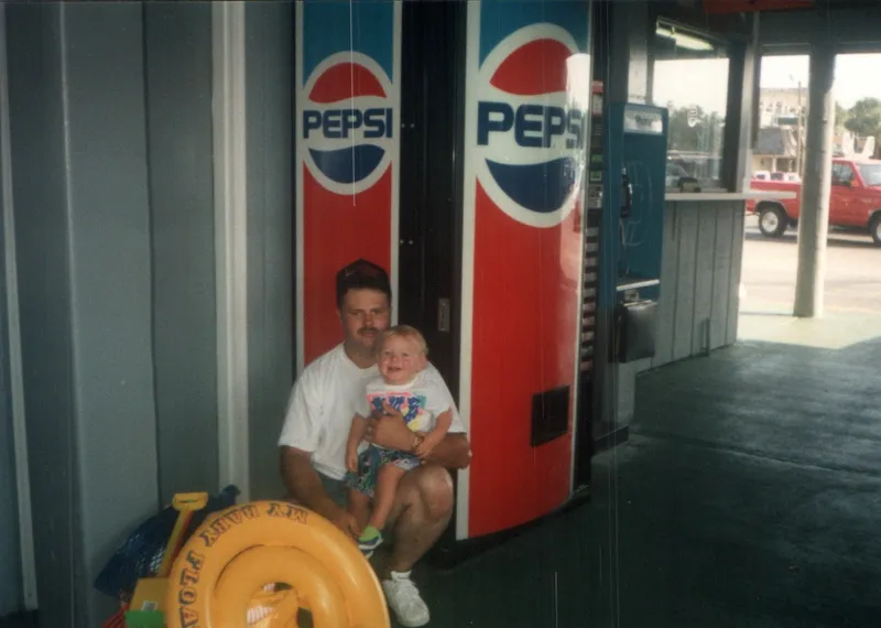 Brian King and a toddler Ryan sitting beside a Pepsi machine