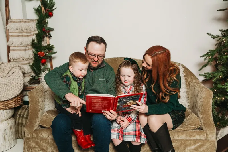Ryan reading a Christmas book to Kamden and Kinsley on a couch with Brittany