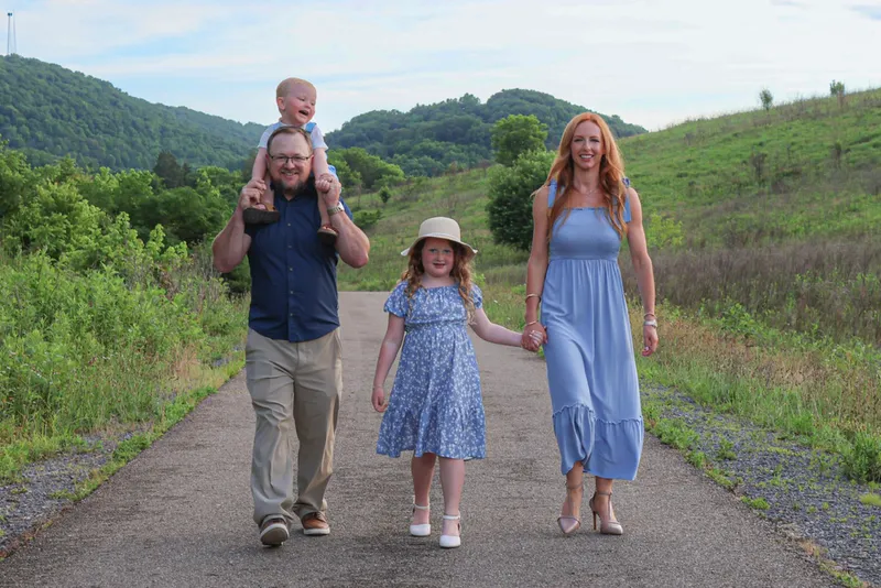 Ryan carrying Kamden on his shoulders while walking a greenway path with Brittany and Kinsley