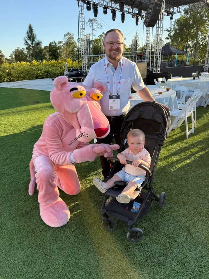 Ryan with Kamden in a stroller next to the Pink Panther mascot at an outdoor event